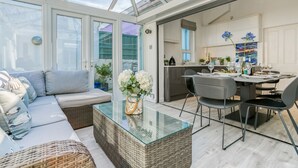 A modern kitchen with a dining area, a glass-top table, and a sofa with cushions. - Ty Haf - sleeps 9 guests  in 5 bedrooms (Rhosneigr)