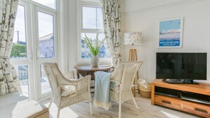 A living room with wicker chairs, a wooden coffee table with a vase of flowers, a television on a wooden stand, and a framed picture on the wall. - Ty Haf - sleeps 9 guests  in 5 bedrooms (Rhosneigr)