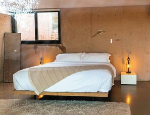 A modern bedroom with a wooden bed frame, white bedding, and a small bedside table with a lamp.