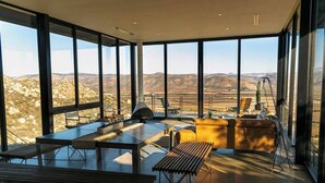 Une pièce spacieuse avec de grandes fenêtres donnant sur le paysage désertique. On y trouve une table à manger avec des chaises, un canapé et un banc.