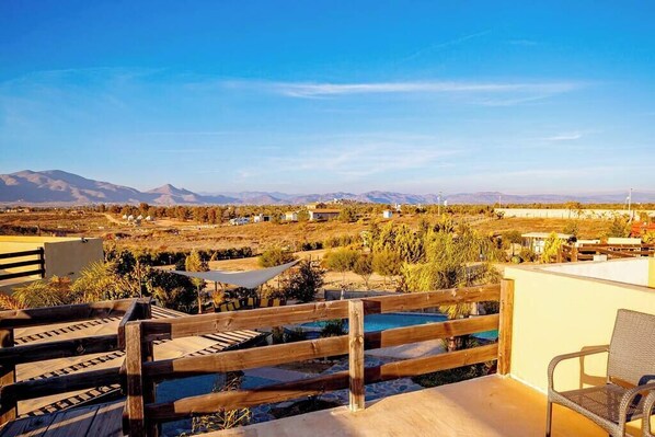 A rooftop terrace with a wooden fence, a pool, and a view of distant mountains.