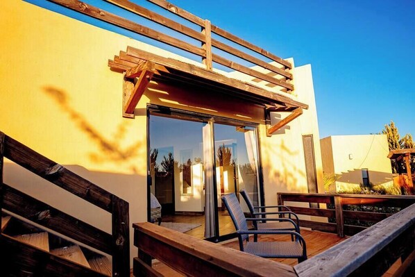 Un patio moderno al aire libre con cubierta de madera, puerta de vidrio y zona de estar con dos sillas.