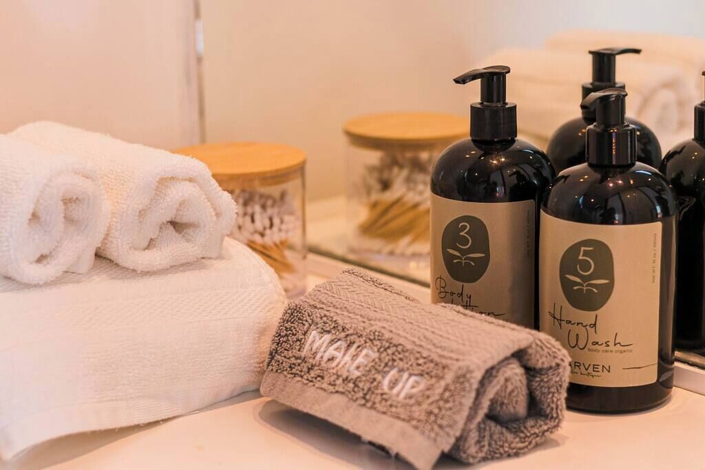 A bathroom with neatly folded towels, a bottle of body wash, and a bottle of shampoo.