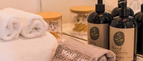 A bathroom with neatly folded towels, a bottle of body wash, and a bottle of shampoo.