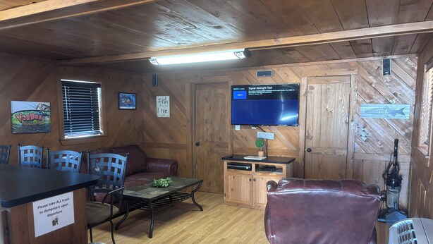 Interior d'una cabana amb terra de fusta, televisió penjada a la paret, sofà, taula i paperera.