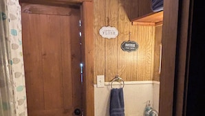 Un bany amb parets de fusta, un lavabo blanc, una tovallola penjada a la paret i una porta amb marc de fusta.