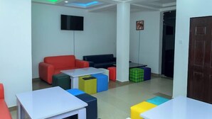 A modern room with a flat-screen TV, colorful seating, and a wooden door. - Oak Up Ultimate Place  (Abuja)