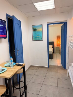 A hotel room with a bed, bedside table, and a desk with a chair. There is a framed picture on the wall and a television mounted on the wall. - AZUR HOTEL (Saint-Denis)