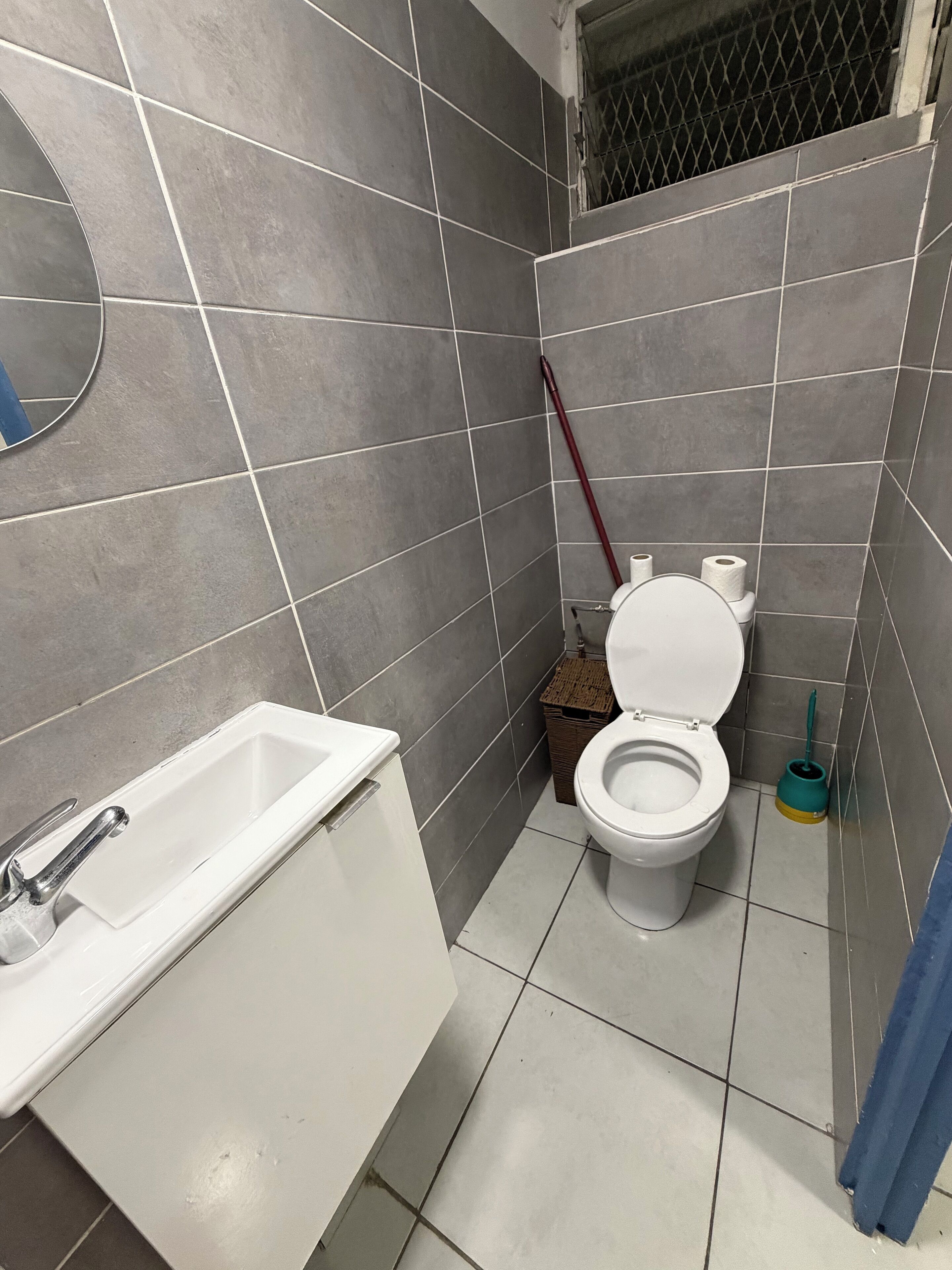 Ein kleines Badezimmer mit einem weißen Waschbecken, einer Toilette und einem Spiegel an der Wand.
