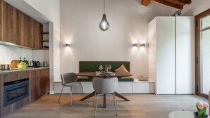 A modern kitchen with wooden cabinetry, a dining area with a round table and two chairs, a built-in bench with cushions, and a hanging light fixture.