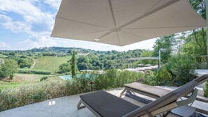 A patio with a lounge chair and umbrella, overlooking a pool and lush greenery.