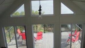 Et værelse med store vinduer, der giver udsigt til en terrasse med røde stole.