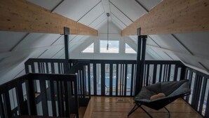 Et hyggeligt loftsværelse med trægulv, en sort stol og udsigt til himlen gennem et ovenlys.