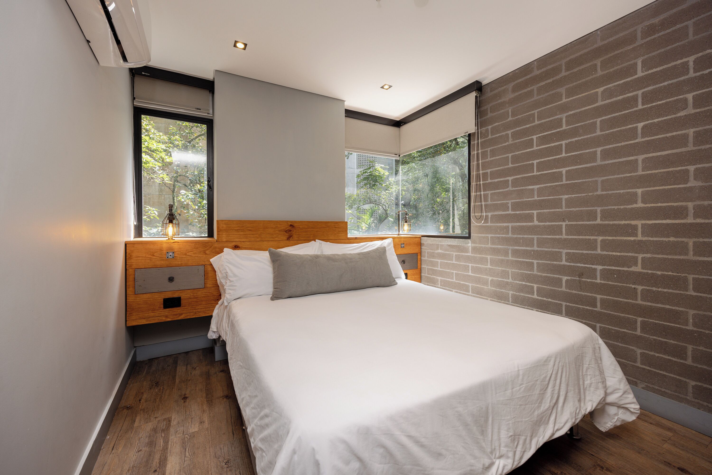 A modern bedroom with a wooden headboard, a large bed, and a brick wall.