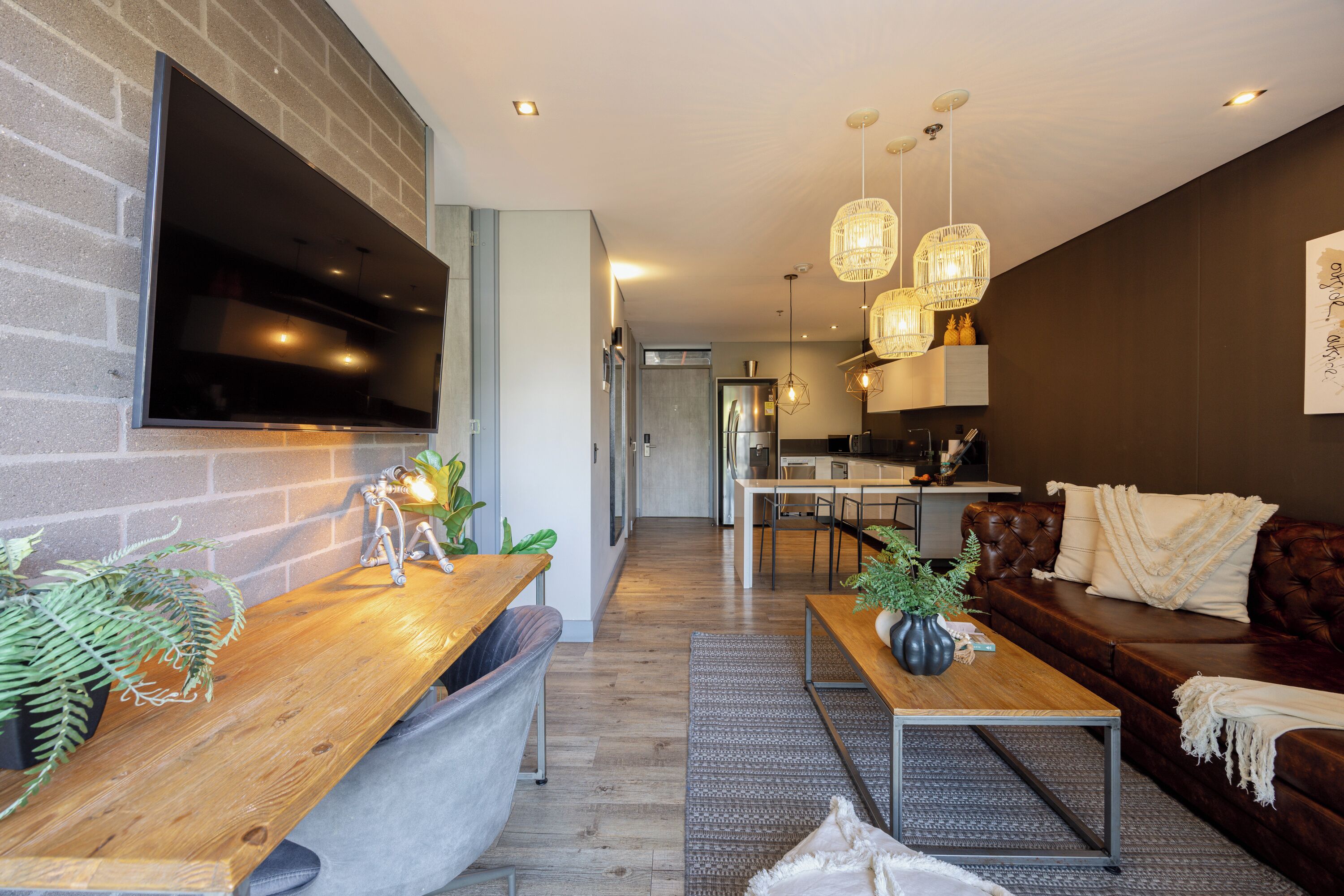 A modern living room with a wooden coffee table, a leather sofa, and a TV mounted on a brick wall.
