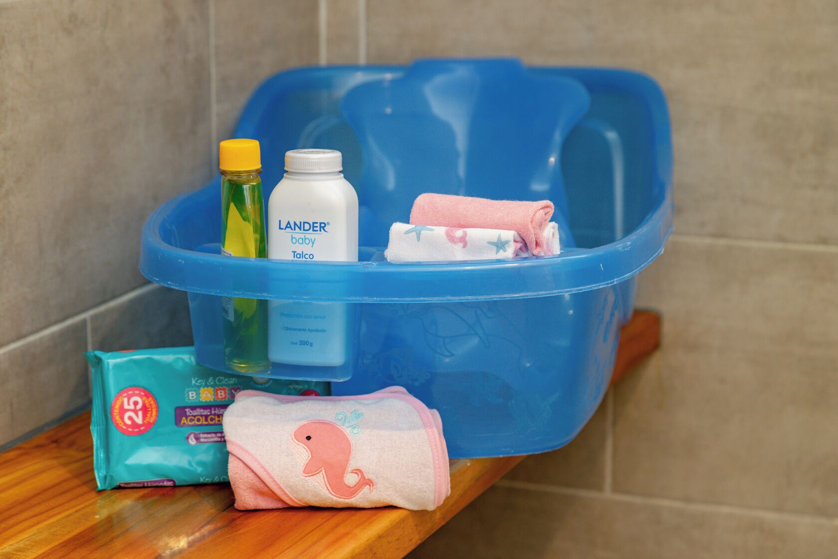 A bathroom with a blue plastic storage bin containing baby products, a bottle of baby lotion, a baby powder container, and a baby wipe pack.