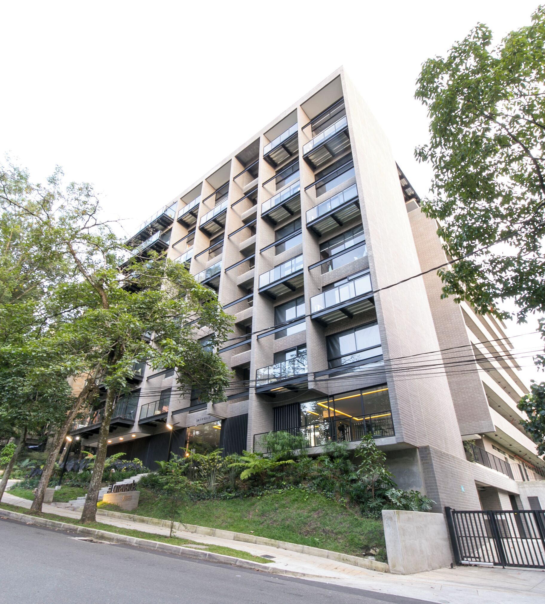 A multi-story building with balconies, a landscaped garden, and a gated entrance.