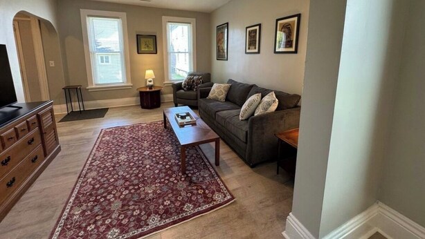 A living room with a sofa, coffee table, and a TV. There are framed pictures on the wall and a window with blinds. - Spacious & Renovated Buffalo Home in 5 Points- Parking, AC, Wifi, and more (Buffalo)