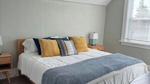 A bedroom with a bed, wooden nightstands, a bedside lamp, a window with blinds, and a patterned rug. - Spacious & Renovated Buffalo Home in 5 Points- Parking, AC, Wifi, and more (Buffalo)