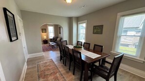 A dining area with a wooden table and chairs, a rug, and a window with blinds. - Spacious & Renovated Buffalo Home in 5 Points- Parking, AC, Wifi, and more (Buffalo)