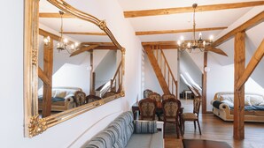 A spacious attic room with exposed wooden beams, a large mirror, a sofa, a dining table, and chairs.