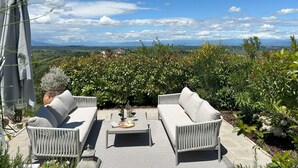 Een terras met uitzicht op een wijngaard en heuvels in de verte.
