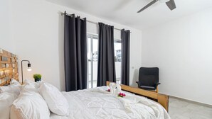 Une chambre d’hôtel moderne avec un grand lit, une tête de lit en bois, un petit bureau et un ventilateur de plafond.
