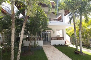 A two-story building with a covered patio area, surrounded by palm trees and a well-maintained lawn. - Coastal Luxury 2-Bed w Pool Access in Bayahibe (Bayahíbe)