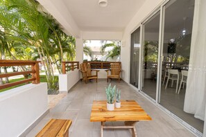 Uma área de estar ao ar livre coberta, com mobiliário de madeira e plantas em vasos.