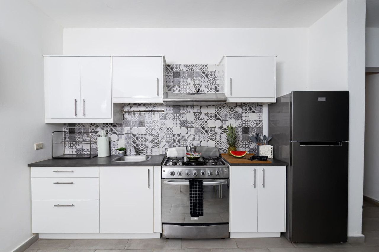 A modern kitchen with white cabinets, a black refrigerator, and a patterned backsplash.