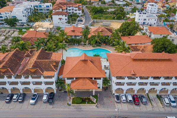 A hotel with a swimming pool, multiple parking spaces, and a red-tiled roof.