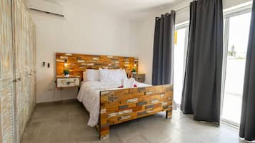 Un dormitorio con cabecera de madera, cama con ropa de cama blanca, mesita de noche con lámpara y ventana con cortinas.