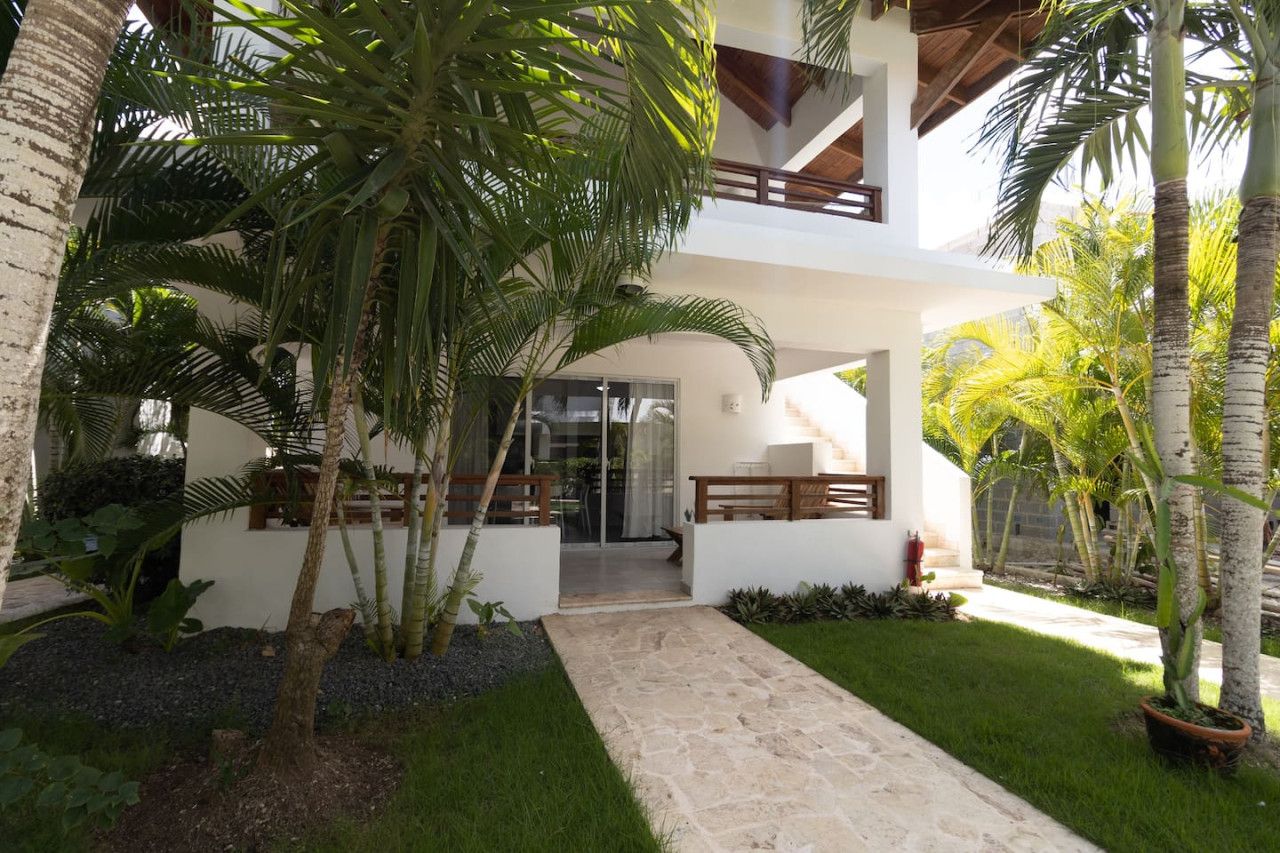 A modern house with a covered patio, palm trees, and a stone pathway leading to the entrance.
