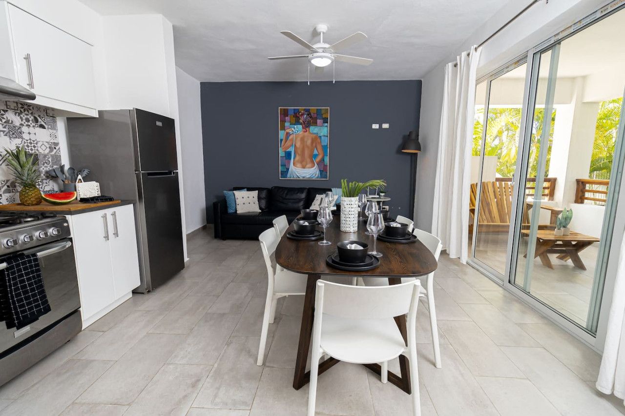 A modern kitchen with white cabinets, a stainless steel refrigerator, and a dining area with a dark wooden table and white chairs.