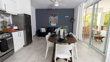 A modern kitchen with white cabinets, a stainless steel refrigerator, and a dining area with a dark wooden table and white chairs.