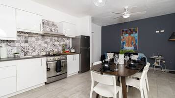 Eine moderne Küche mit weißen Schränken, einem Edelstahl-Kühlschrank und einem Essbereich mit Holztisch und weißen Stühlen.