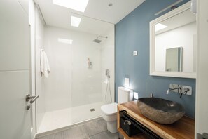 A modern bathroom with a glass shower enclosure, a white toilet, and a wooden vanity with a stone sink. - Kyuka Surfclub (La Oliva)
