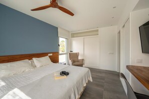 A modern bedroom with a large bed, a ceiling fan, a chair, and a TV. - Kyuka Surfclub (La Oliva)