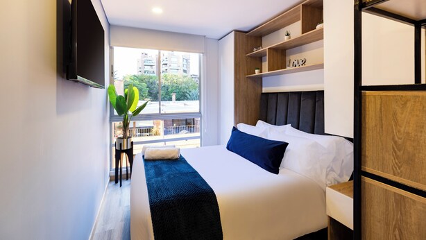 A modern hotel room with a large bed, a TV mounted on the wall, and a view of the city through the window. - Comfortable Loft in Zona T w/ Fast Wi-fi (BOGOTA)