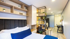 A modern hotel room with a bed, a wooden headboard, a built-in shelf with plants, a small table with a bottle, and a desk with a chair. - Comfortable Loft in Zona T w/ Fast Wi-fi (BOGOTA)