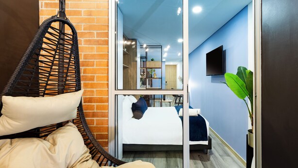 A modern hotel room with a hanging chair, a bed with pillows, a TV, and a plant. - Exclusive Loft w/ Terrace In Zona T w/ Fast Wi-Fi (BOGOTA)