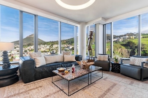 A modern living room with a large window, a sectional sofa, a coffee table, and a view of a town and hills.