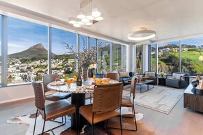Un espace repas moderne avec une grande table, des chaises et une vue sur la ville et les montagnes.