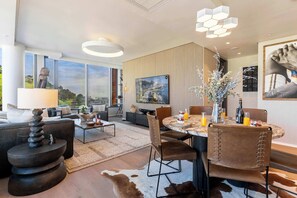 Ett modernt vardagsrum med en matplats, stora fönster, en öppen spis och en tavla som föreställer en stadsbild.