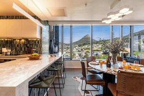 A modern kitchen with a marble countertop, bar stools, and a dining area with a table set for breakfast.