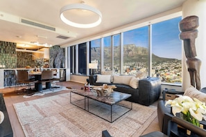 A modern living room with a large window, a dining area, and a kitchen.