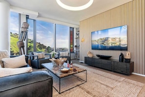 Una sala de estar moderna con un televisor grande, asientos cómodos y vistas al exterior.