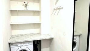 Una sala de lavandería con lavadora, estanterías y un espejo.