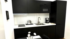 Una cocina compacta con gabinetes negros, una encimera blanca, un fregadero y una cafetera.