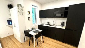 Una cocina compacta con armarios negros, un microondas, una cafetera y un pequeño comedor con dos sillas.